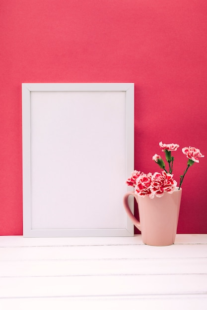 Carnation flower vase with empty photo frame on white wooden table