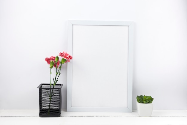 Carnation flowers pot and succulent plant with empty frame at home