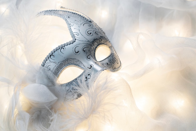 Foto gratuita maschera di carnevale posizionata su tessuto bianco e luci sotto