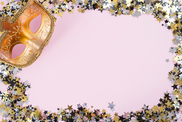 Карнавальная маска с маленькими блестками на розовом столе