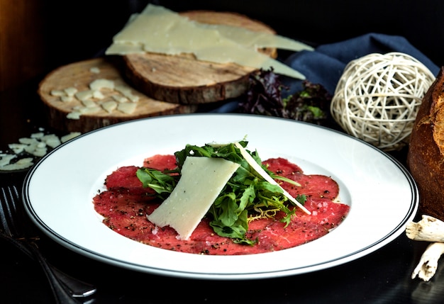 Foto gratuita fette di carpaccio condite con rucola e fetta di parmigiano