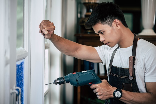 Foto gratuita il carpentiere tiene il trapano e perfora la finestra.