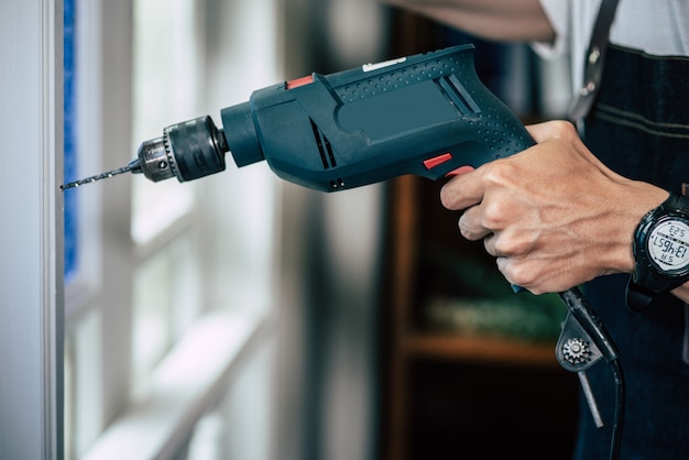 The carpenter holds the drill and drills the window.