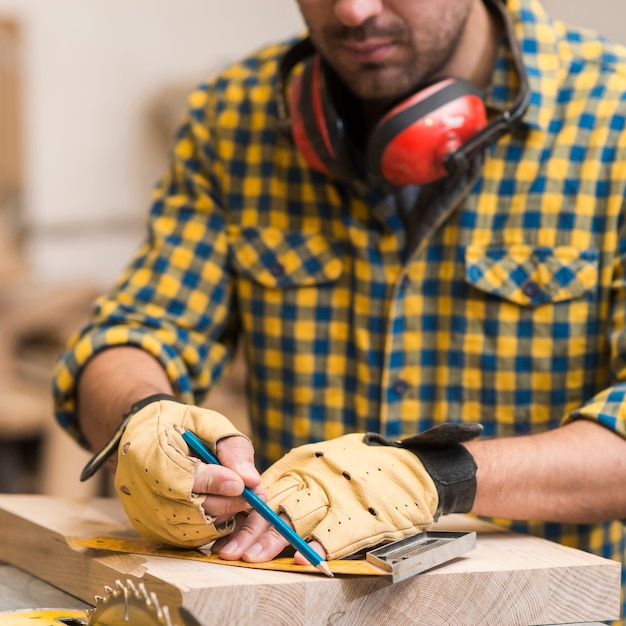 Carpenter measuring and tracing lines with a ruler on a wooden surface