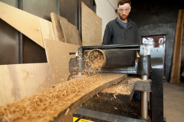 Carpenter operating stationary power planer, processing wooden plank, making sawdust
