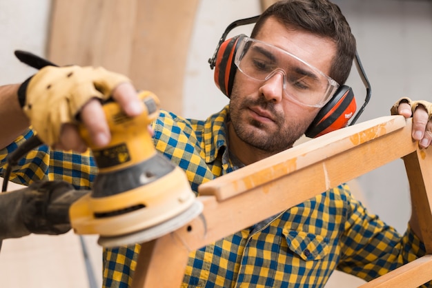 Carpenter softening edges of wooden furniture with electric sander