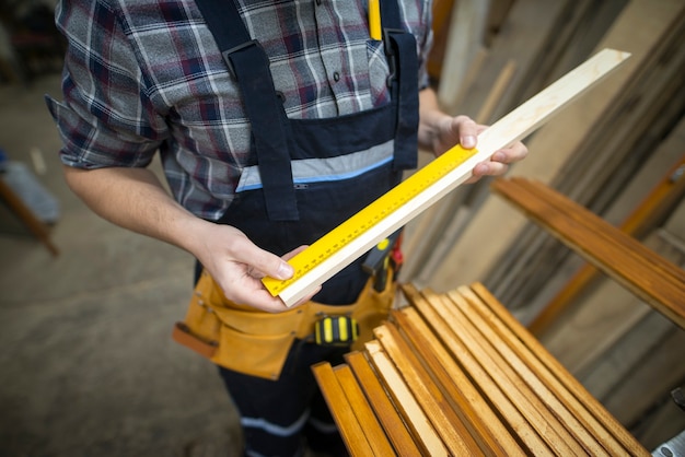 Бесплатное фото Плотник измеряет доску, которую он собирается распилить в деревообрабатывающей мастерской