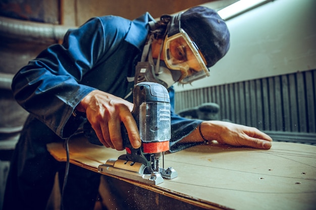 Carpenter using circular saw for cutting wooden boards. Construction details of male worker or handy man with power tools