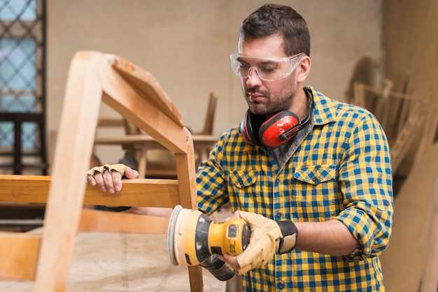 The carpenter works with the electric polisher on the wood