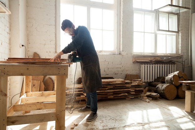 Carpentry workshop. Man using electric hand saw on wooden planks