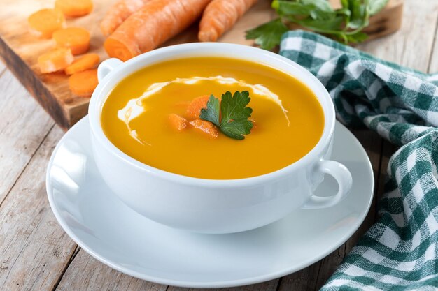 Carrot soup with cream and parsley on wooden table Close up