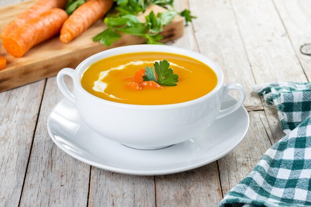 Carrot soup with cream and parsley on wooden table