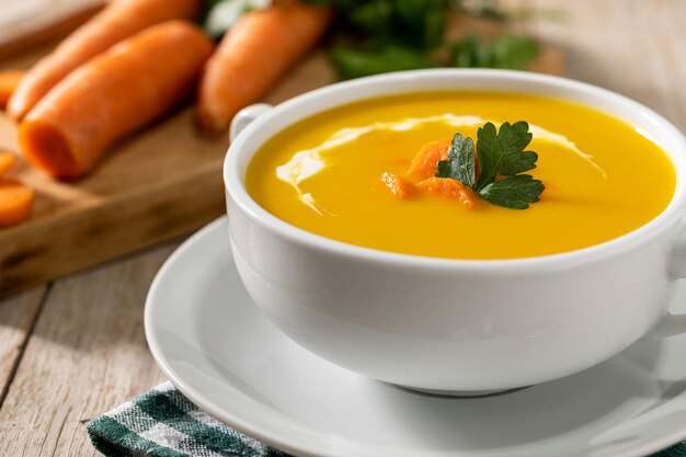 Carrot soup with cream and parsley on wooden table