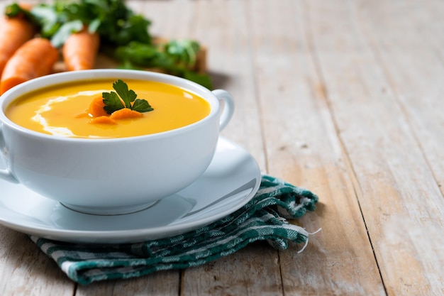Carrot soup with cream and parsley on wooden table