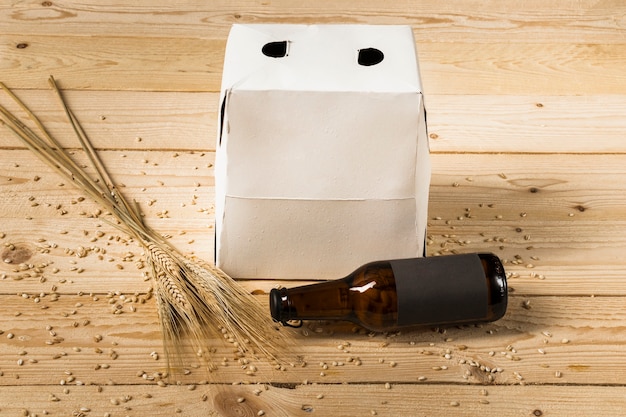 Картонная коробка; пивная бутылка и колосья пшеницы на деревянной поверхности