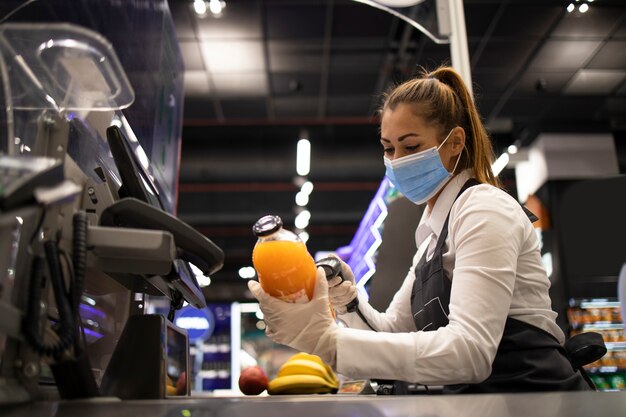 コロナウイルスから完全に保護されたマスクと手袋を着用した食料品店のレジ係