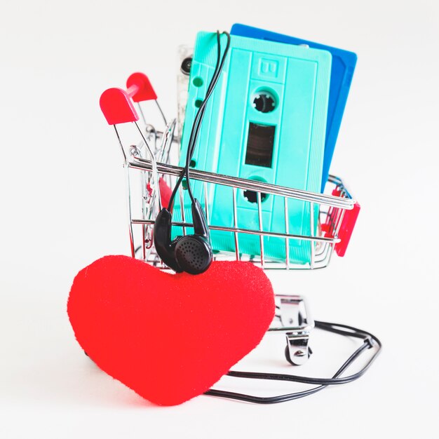 Cassette tapes in shopping trolley with earphone and red heart against white backdrop