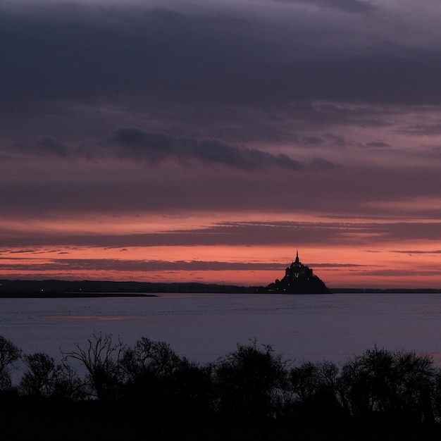 Foto gratuita castello di fronte all'oceano sotto un cielo velato durante il tramonto