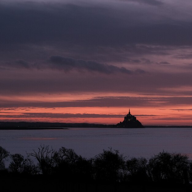 Castle in front of the ocean under a clouded sky during sunset