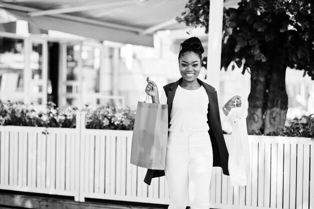 屋外を歩く色付きの買い物袋を持つカジュアルなアフリカ系アメリカ人の女の子スタイリッシュな黒人女性の買い物