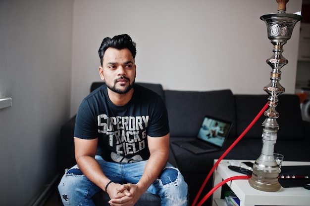 Случайный бородатый индийский мужчина сидит в комнате против кальяна