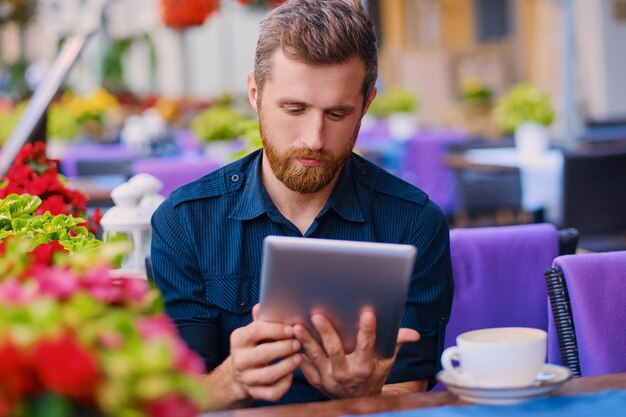 カジュアルなあごひげを生やした男性がコーヒーを飲み、カフェでタブレットPCを使用しています。