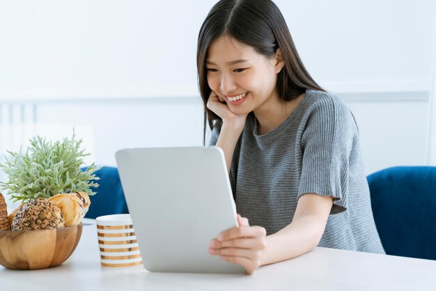 Casual beautiful asian woman enjoy weekend morning withn tea and tablet white room interior background