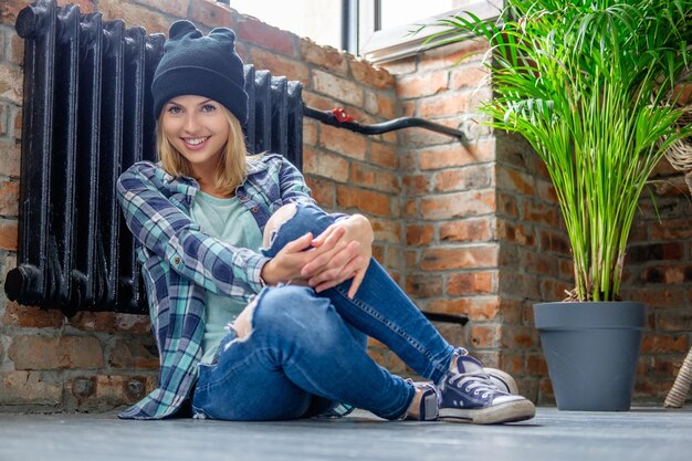 Casual blond female in denim jeans posing on a floor in living room.