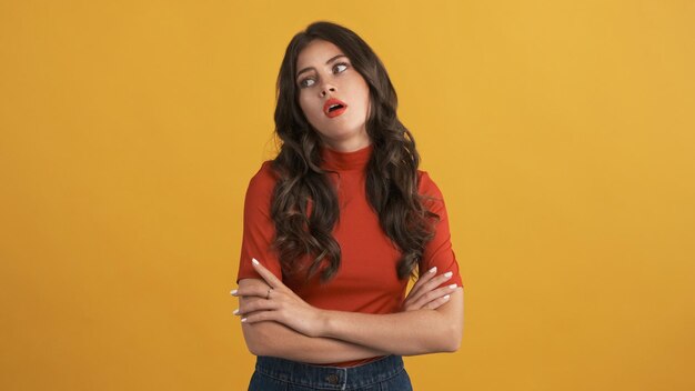Casual bored brunette girl in red top with hands crossed tiredly posing on camera over yellow background Not interested expression