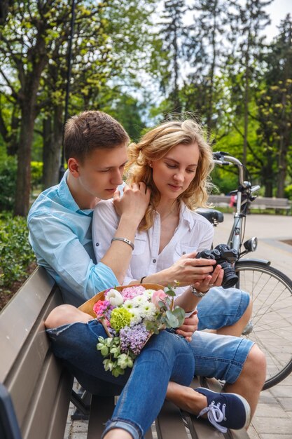 Casual couple using compact dslr photocamera in summer park.