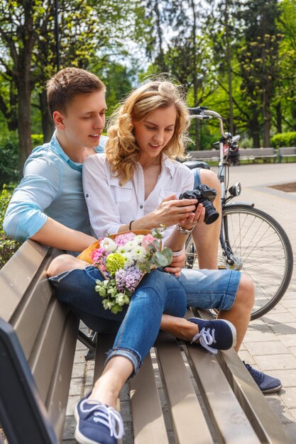 Casual couple using compact dslr photocamera in summer park.