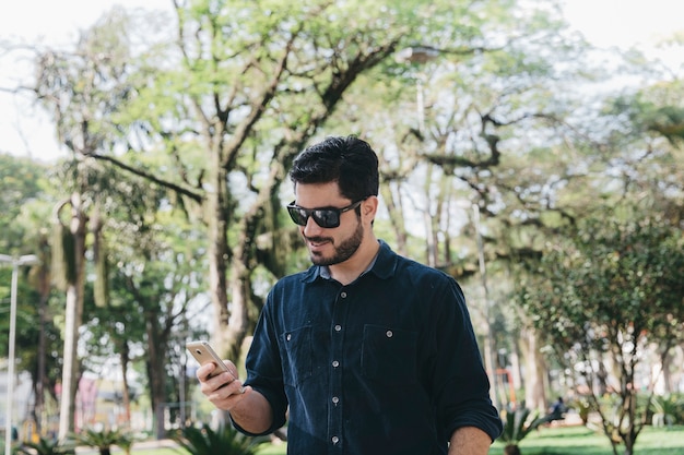 Foto gratuita uomo casuale che utilizza telefono nel parco