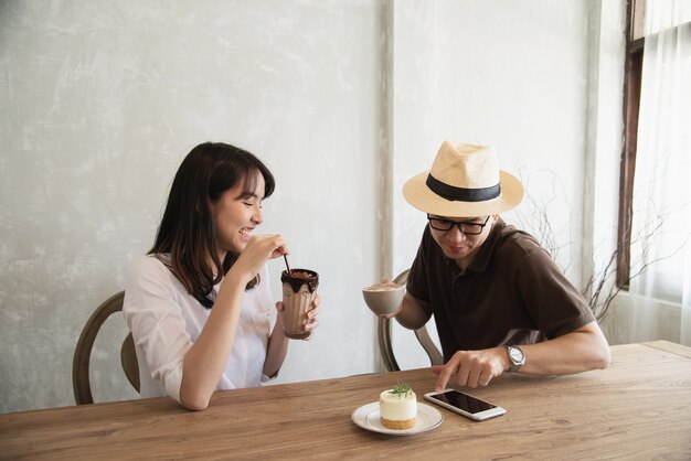 Casual man and woman talking happily while drink coffee and looking mobile phone 