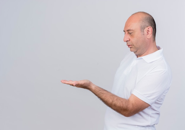 Casual mature businessman standing in profile view showing empty hand and looking at it isolated on white background with copy space
