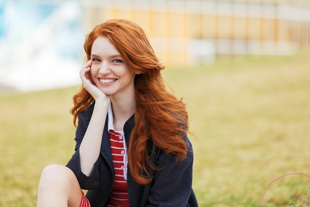 公園の芝生の上に座っているカジュアルな赤い頭の女性