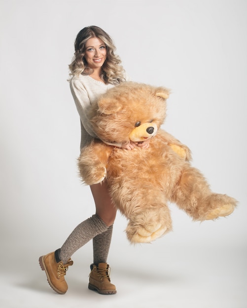Casual smiling young woman in knitted clothes holding big soft teddy bear