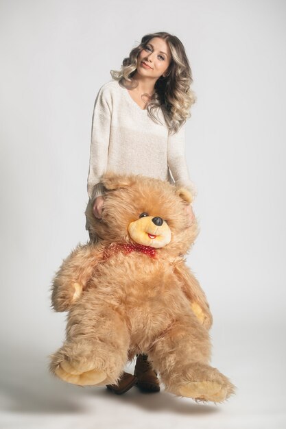 Casual smiling young woman in knitted clothes holding big soft teddy bear