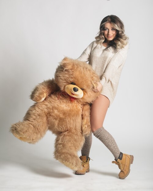 Casual smiling young woman in knitted clothes holding big soft teddy bear