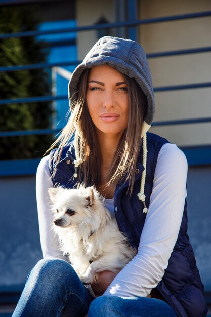 Casual woman holding small white dog. Nature lights