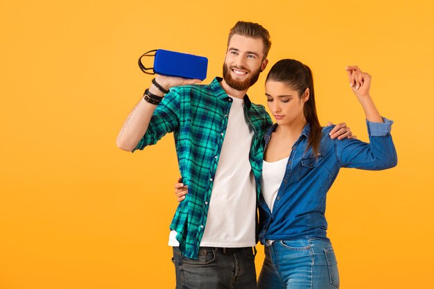 Casual young couple holding wireless speaker happy listening to music dancing colorful style happy mood isolated on yellow wall