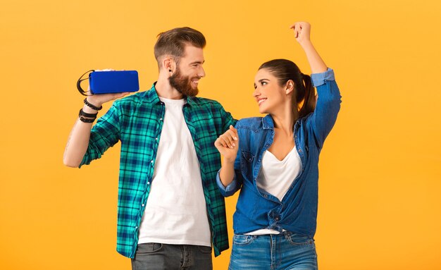 Casual young couple holding wireless speaker listening to music dancing on orange