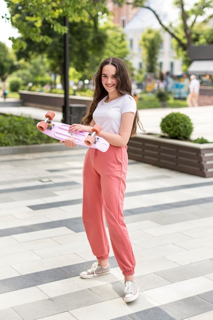 Casual young girl holding her skateboard outside