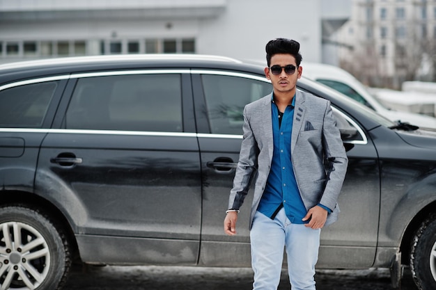 Casual young indian man in sunglasses posed against suv car