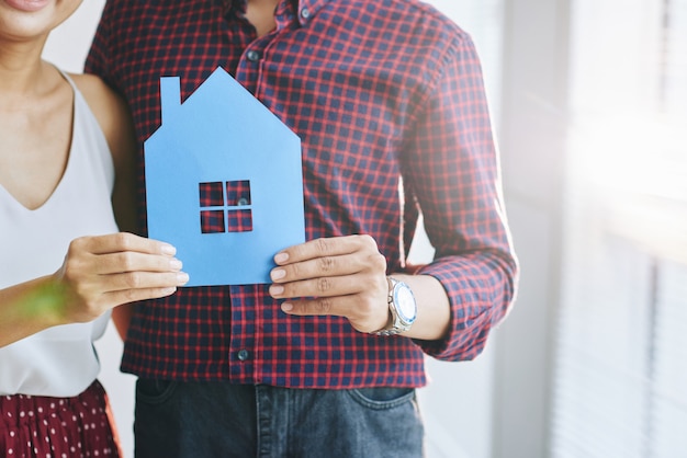 Free photo casually dressed unrecognizable couple hugging and posing with paper cutout of house