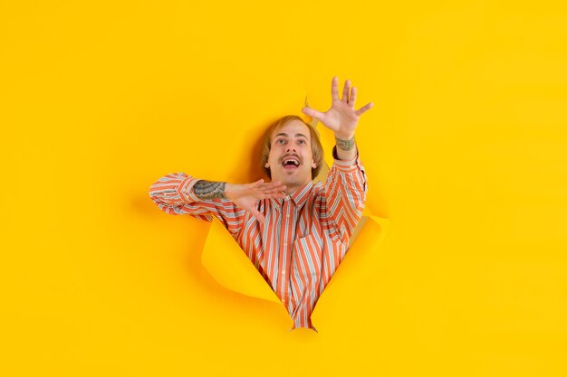 Catching something. Cheerful caucasian young man poses in torn yellow paper, emotional and expressive.