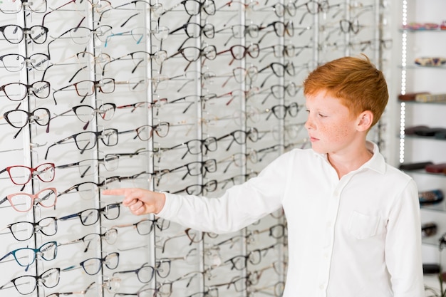 Caucasian boy pointing index finger at eyeglasses rack