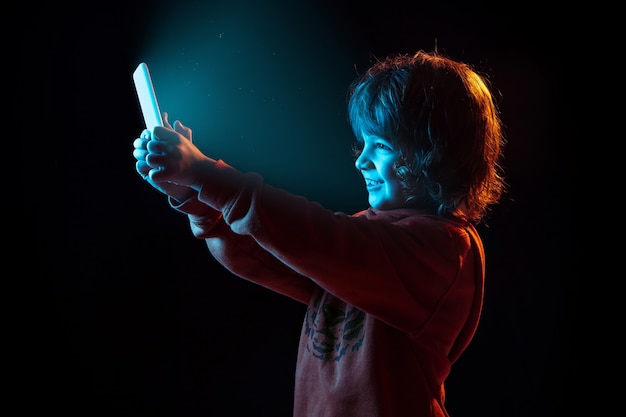 Портрет кавказского мальчика изолирован на темной студии в неоновом свете