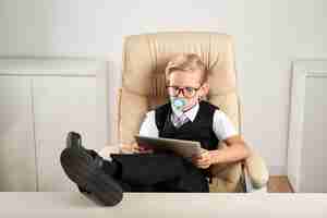 Free photo caucasian boy sitting in executive chair in office with dummy in mouth and using tablet