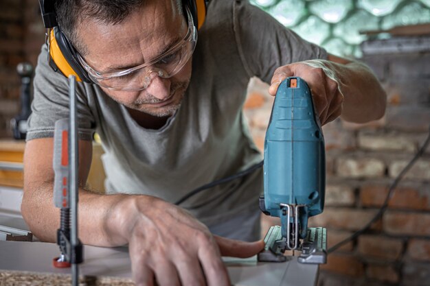 Кавказский плотник занимается пилением дерева лобзиком в своей мастерской.
