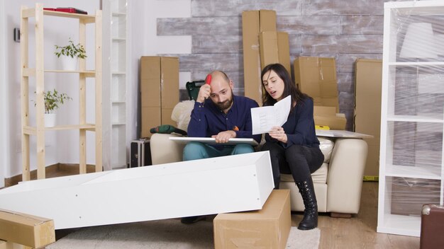 Caucasian couple arguing while assembling a shelf in their new apartment. Girlfriend holding instructions.